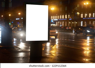 The Billboard Lightposter, Ad CityLight Shines In The Night City. Mockup With A White Field For Advertising. Rainy Evening, Wet Weather And Road