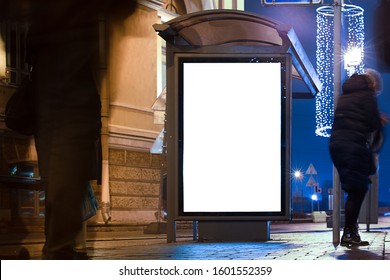 Billboard In A Stop. White Field For Advertising Glowing At Night In The City. Vertical Field Mockup. With People In The Background