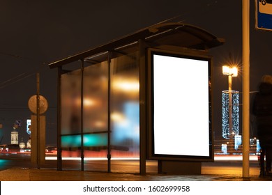 Billboard In A Stop. White Field For Advertising Glowing At Night In The City. Vertical Field Mockup Glass Stop Passing By Blurry Cars With People In The Background