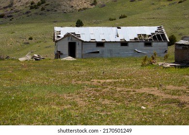 Billings, MT United States 05 22 2022

A Dilapidated White House With Holes In The Roof And No Windows Standing In A Green Field With Brown Patches. 