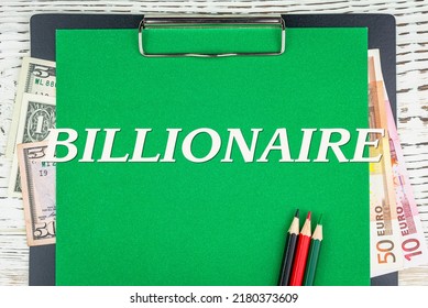 BILLIONAIRE - Word (text) Euro And Dollar Bills On A Green Background, Colored Pencils And A Wooden White Table. Business Concept: Buying, Selling, Commerce (copy Space).