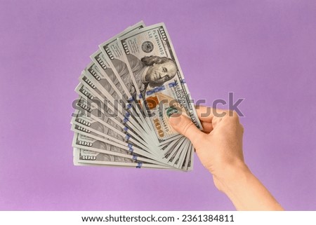 A lot of bills of 100 dollars in hands are folded in a fan on a purple background. Currency, banknotes in female hands. The concept of success, business, wealth.