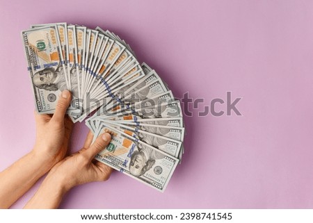 A lot of bills of 100 dollars in hands are folded in a fan on a pink background. Currency, banknotes in female hands. The concept of success, business, wealth.