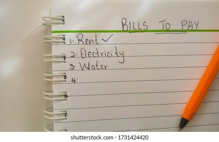 Bills To Pay Checklist. Rent, Electricity And Water Written On A Notepad. Orange Pen. Space. 