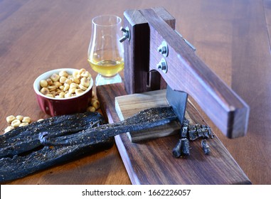 Biltong being cut with a biltong cutter with a glass of whiskey and a bowl of toasted corn.