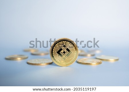 Binance BNB cryptocurrency coin standing centrally placed among bunch of crypto gold coins on blue background. Close-up, soft focus.