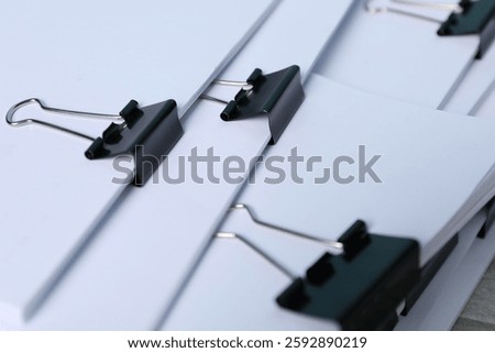 Binder clips with sheets of paper as background, closeup