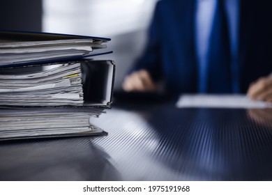 Binders with papers are waiting to be processed by man accountant in blue blazer staying at home during covid pandemic. Taxes and audit concept. Internal Revenue Service inspector checking financial