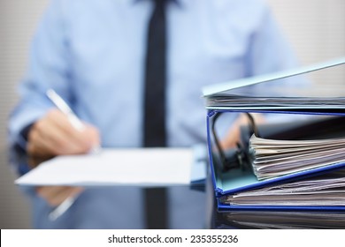 binders with papers are waiting to be processed with businessman  back in blur. Accounting and business concept