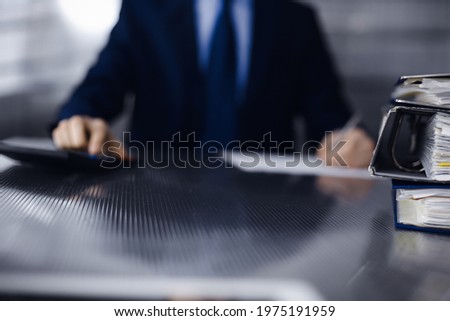 Binders with papers are waiting to be processed by man accountant in blue blazer staying at home during covid pandemic. Taxes and audit concept. Internal Revenue Service inspector checking financial