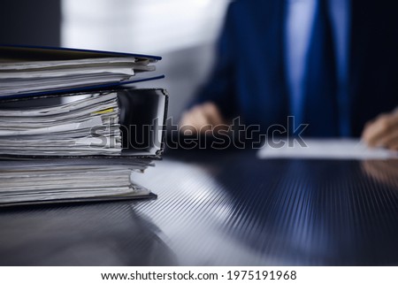 Binders with papers are waiting to be processed by man accountant in blue blazer staying at home during covid pandemic. Taxes and audit concept. Internal Revenue Service inspector checking financial