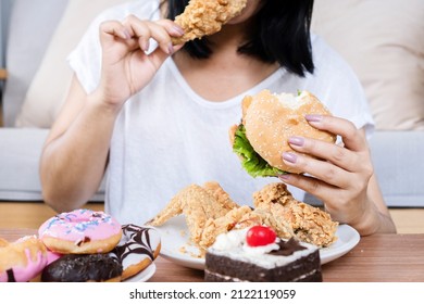 Binge eating disorder concept with woman eating fast food burger, fired chicken , donuts and desserts  - Shutterstock ID 2122119059