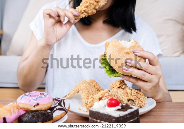 Binge eating disorder\
concept with woman eating fast food burger, fired chicken , donuts\
and desserts 