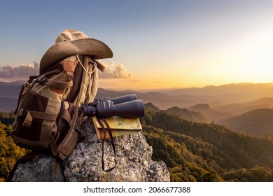 Binocular with map paper and hiker hat and backpack on top of rock mountain at sunset