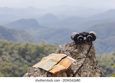 Binoculars And Map Paper On Top Of The Rock Mountain