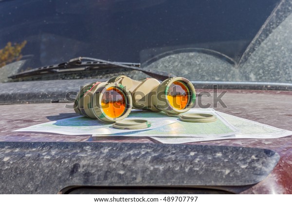 binoculars with maps on the bonnet lies a brutal\
dirty off-road car. navigattsiya orienteering tourism travel\
off-road