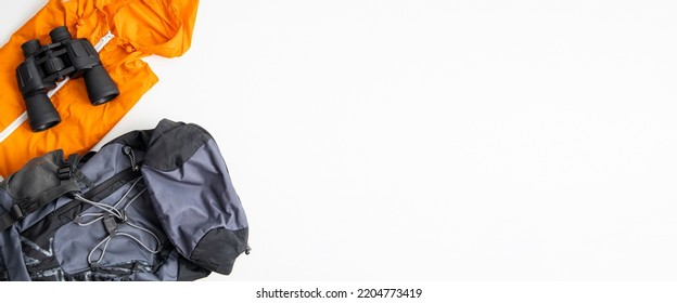 Binoculars, tourist backpack, raincoat on a white background. Top view, flat lay. Banner. - Powered by Shutterstock