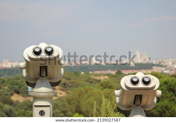 BINOCULARS FROM A VIEWPOINT IN\
A PARK WITH THE CITY PANORAMA IN THE BACKGROUND AND SOME CABLE CAR\
CABINS