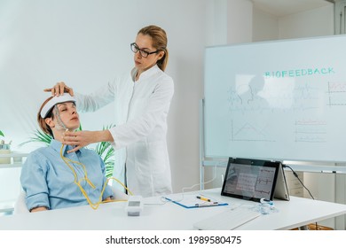 Biofeedback EEG Or Electroencephalograph Training At A Health Center. Therapist Monitoring Brain Waves Using Scalp Sensors Placed Onto A Client’s Head 