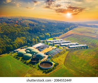 Biogas plant and farm in green fields against sunset. Renewable energy from biomass. Aerial view to modern agriculture in Czech Republic and European Union. 