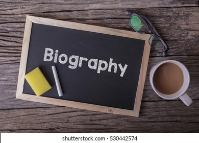 Biography On Blackboard With Cup Of Coffee, With Glasses On Wooden Background