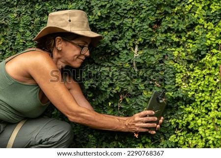 biologist woman in glasses and hat and green clothes, photographing insects in the middle of nature