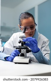 Biologist woman working at vaccine development analyzing blood sample using medical microscope in biochemistry hospital laboratory. Chemist researcher doctor searching for healthcare treatment