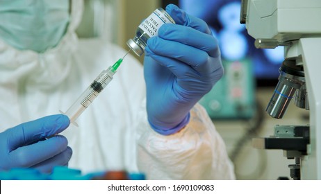 A biomedical research laboratory scientist in full personal protective garb or PPE using a syringe to extract a sample from a vial with a trial or potential vaccine for COVID19. - Shutterstock ID 1690109083