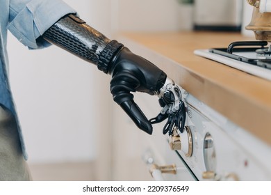 Bionic Prosthetic Arm Adjusting Temperature On Gas Hob Control Panel, Person With Disability Using Stove By Artificial Robotic Hand, Close-up. Domestic Life Routine And People With Disabilities.