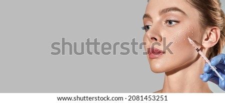 Biorevitalization procedure. Pretty woman while beauty injections with hyaluronic acid for smoothing of mimic wrinkles around eyes, over grey background with space for text