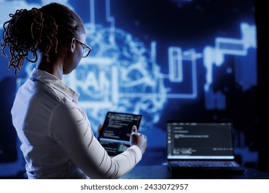 BIPOC engineer updating neural networks made up of interconnected nodes, writing intricate binary code scripts on laptop and tablet. Computer operator using programming to upgrade AI simulation model