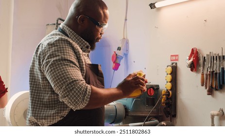 BIPOC man in studio with woodworking tools in background using sandpaper for sanding wooden surface. Woodworking expert using abrasive sponge to fix damages suffered by piece of wood, camera A - Powered by Shutterstock