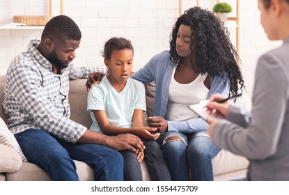 Bipolar Disorder In Children Concept. Little African American Girl And Her Parents At Reception Of Psychologist, Kid Sharing Her Feelings With Doctor