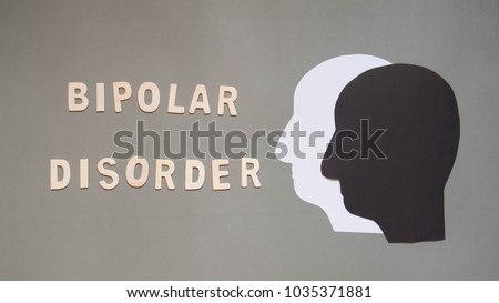 Bipolar disorder presented by double human head made from black and white paper on gray background w/ wood word. Manic and depress emotion. Mental health, brain disorder and psychological concept.