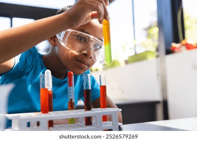 Biracial boy engaged in a science experiment at school in the classroom with copy space. Safety goggles on, he carefully examines a test tube, showcasing a hands-on learning experience. - Powered by Shutterstock