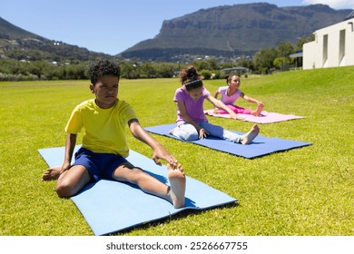 Biracial boy and girls practice yoga on mats in a sunny park. The children, dressed in colorful sportswear, are engaged in a stretching exercise outdoors. - Powered by Shutterstock