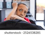 Biracial boy looks thoughtful in a classroom setting at school. His expression suggests contemplation or daydreaming during a school activity.