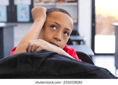 Biracial boy looks thoughtful in a classroom setting at school. His expression suggests contemplation or daydreaming during a school activity. - Powered by Shutterstock