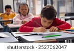 A biracial boy in red draws with focus. A black boy and biracial girl work behind him, showing normal school day, unaltered