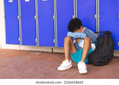 Biracial boy sits alone at school, with copy space. He appears upset, sitting by lockers with his head down. - Powered by Shutterstock