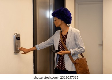 Biracial casual businesswoman with blue afro holding smartphone and calling elevator in office. Casual office, business, communication and work, unaltered. - Powered by Shutterstock