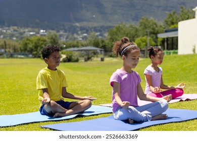 Biracial children practice yoga outdoors, with mountains in the background. Two girls, one 9 and the other 10, and an 8-year-old boy focus on their poses on a sunny day. - Powered by Shutterstock