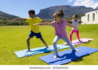 Biracial children practice yoga outdoors on a sunny day. They are focused on their poses, with a mountainous backdrop enhancing the serene setting. - Powered by Shutterstock