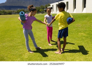 Biracial children are preparing for a yoga session outdoors on a sunny day. Two girls and a boy, all smiling, stand on grass with yoga mats, ready for exercise. - Powered by Shutterstock