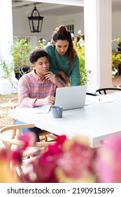 Biracial Couple On Garden Terrace Outside House Using Laptop, Drinking Coffee And Paying Bills. Inclusivity, Domestic Life And Togetherness Concept.