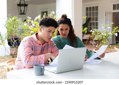 Biracial couple sitting on garden terrace outside house using laptop and paying bills. Inclusivity, domestic life and togetherness concept. - Powered by Shutterstock