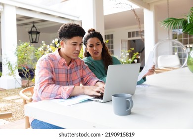 Biracial Couple Sitting On Garden Terrace Outside House Using Laptop And Paying Bills. Inclusivity, Domestic Life And Togetherness Concept.