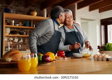 Biracial elderly couple happily cooking in the modern kitchen. Husband kissing wife on the cheek, healthy retired. - Powered by Shutterstock