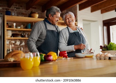 Biracial elderly couple laughing happily cooking in the kitchen. Husband's arm around wife, healthy retired lifestyle. - Powered by Shutterstock