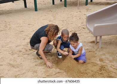 Biracial Family Woman Preschool Age Boy Toddler Girl Playing With Sand On Playground